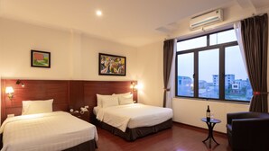 Quarto de hotel com duas camas, uma mesinha com uma garrafa, uma cadeira e uma janela grande com cortinas.
