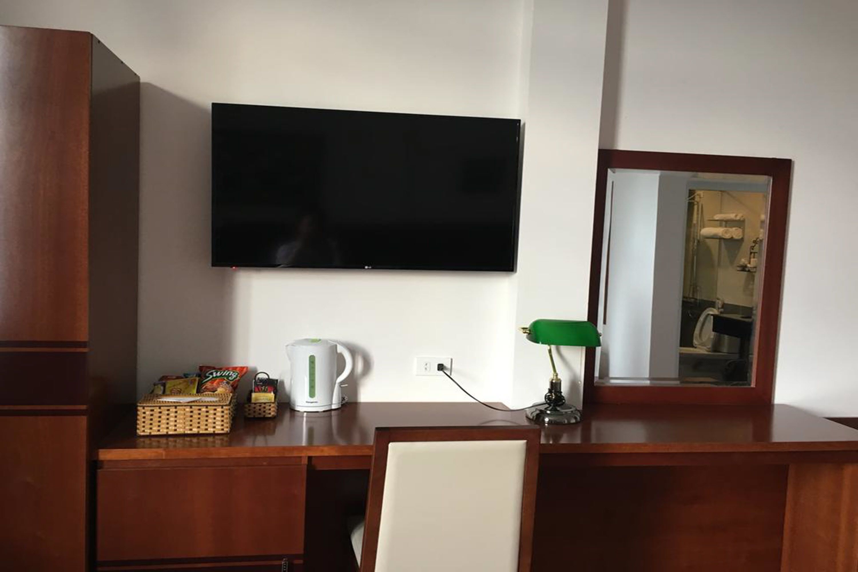 Ein Zimmer mit Flachbildfernseher an der Wand, einem Holztisch mit Wasserkocher, Lampe und einer Korb voller Snacks.
