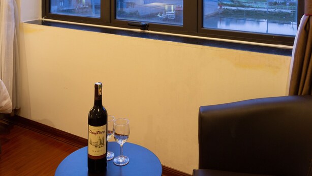 Um quarto com uma grande janela, uma garrafa de vinho, duas taças e uma cadeira.