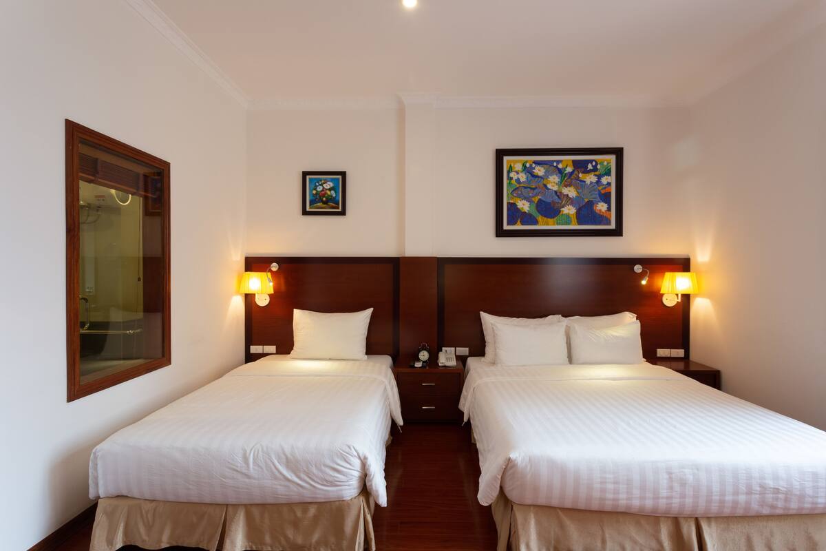Habitación de hotel con dos camas, una mesita de noche, un espejo y dos lámparas de pared.