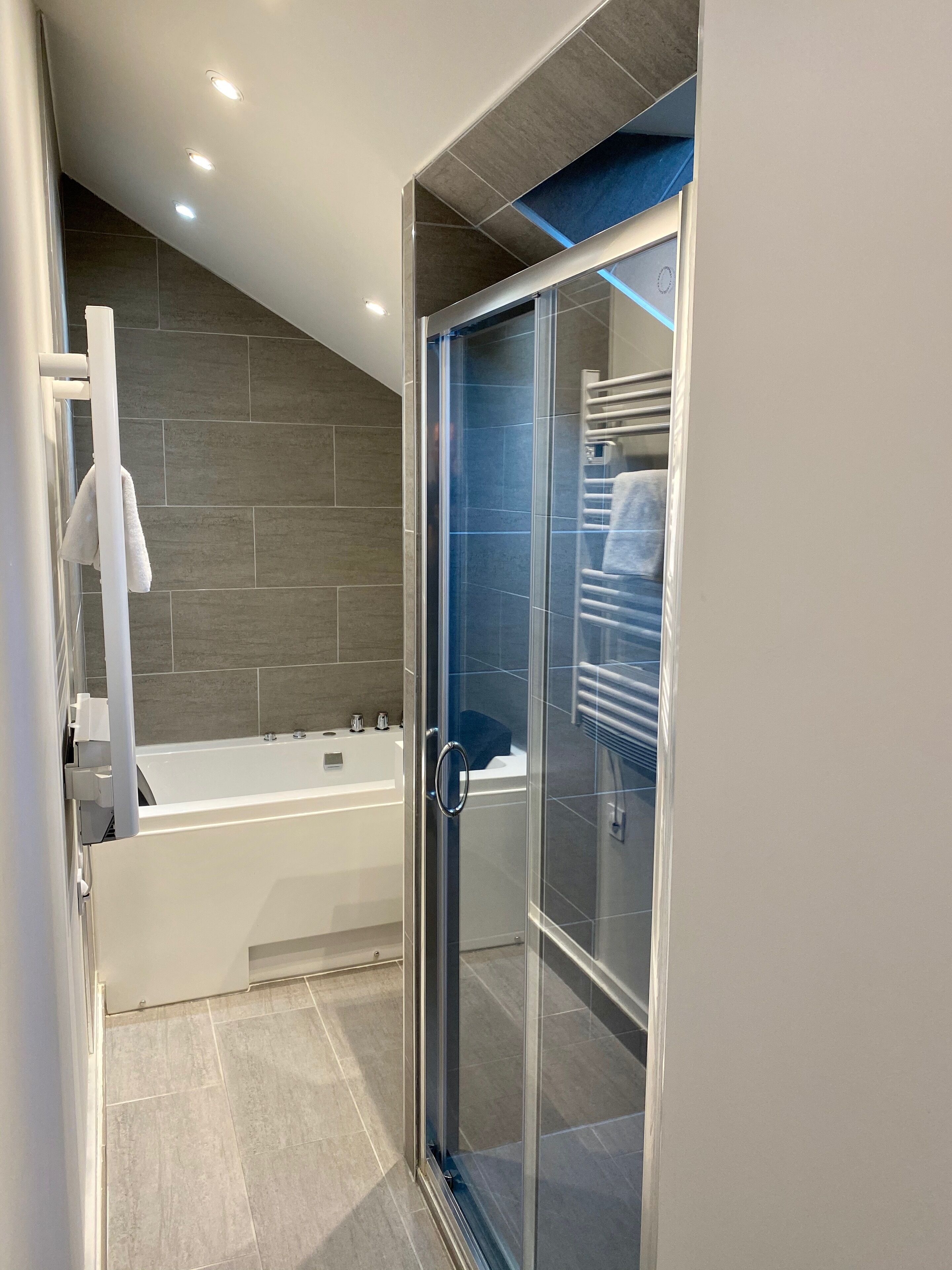 Een moderne badkamer met een douchecabine van glas, een witte badkuip en een handdoekhouder.