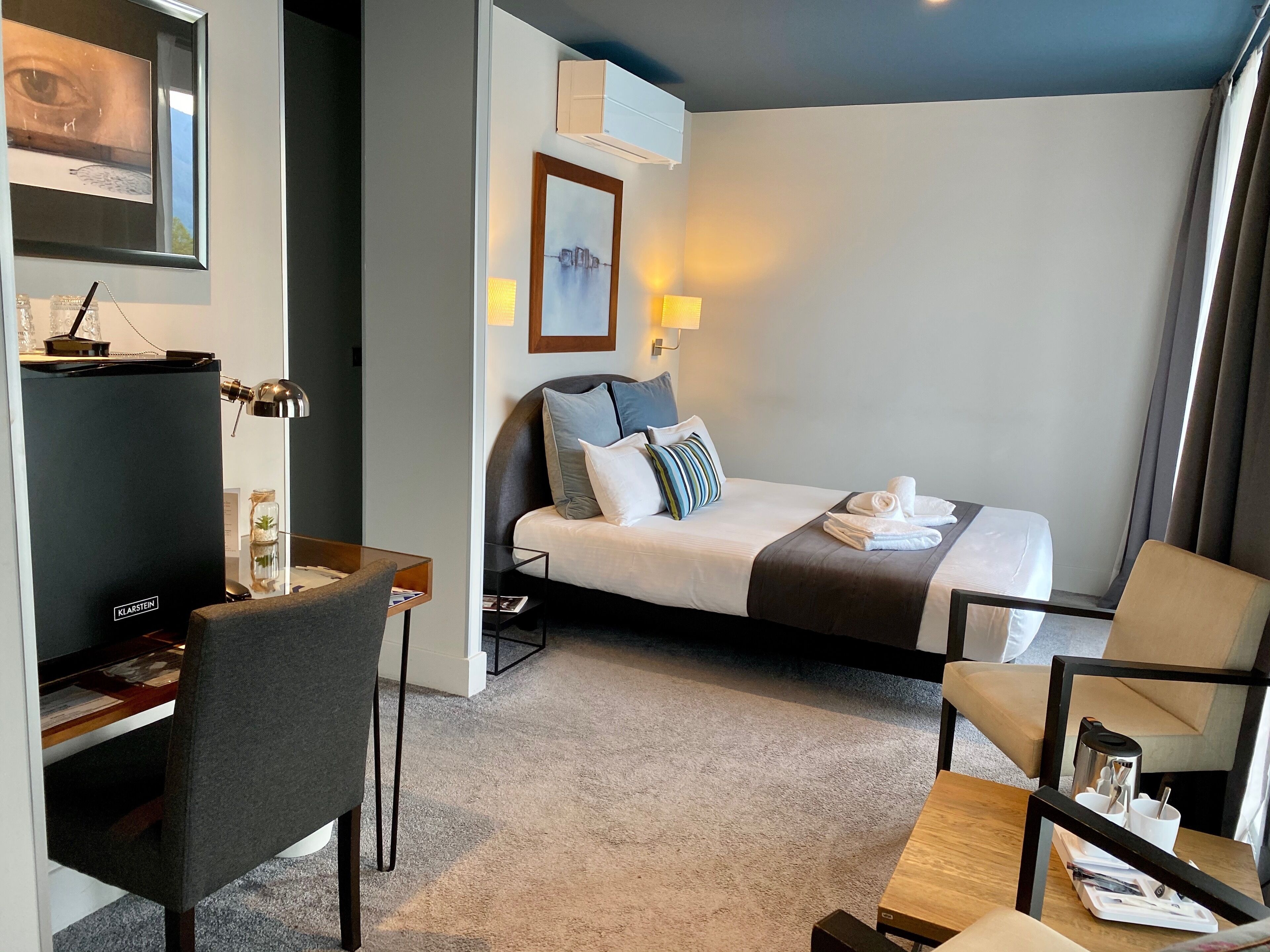 Quarto de hotel com cama, escrivaninha, cadeira, televisão e abajur.