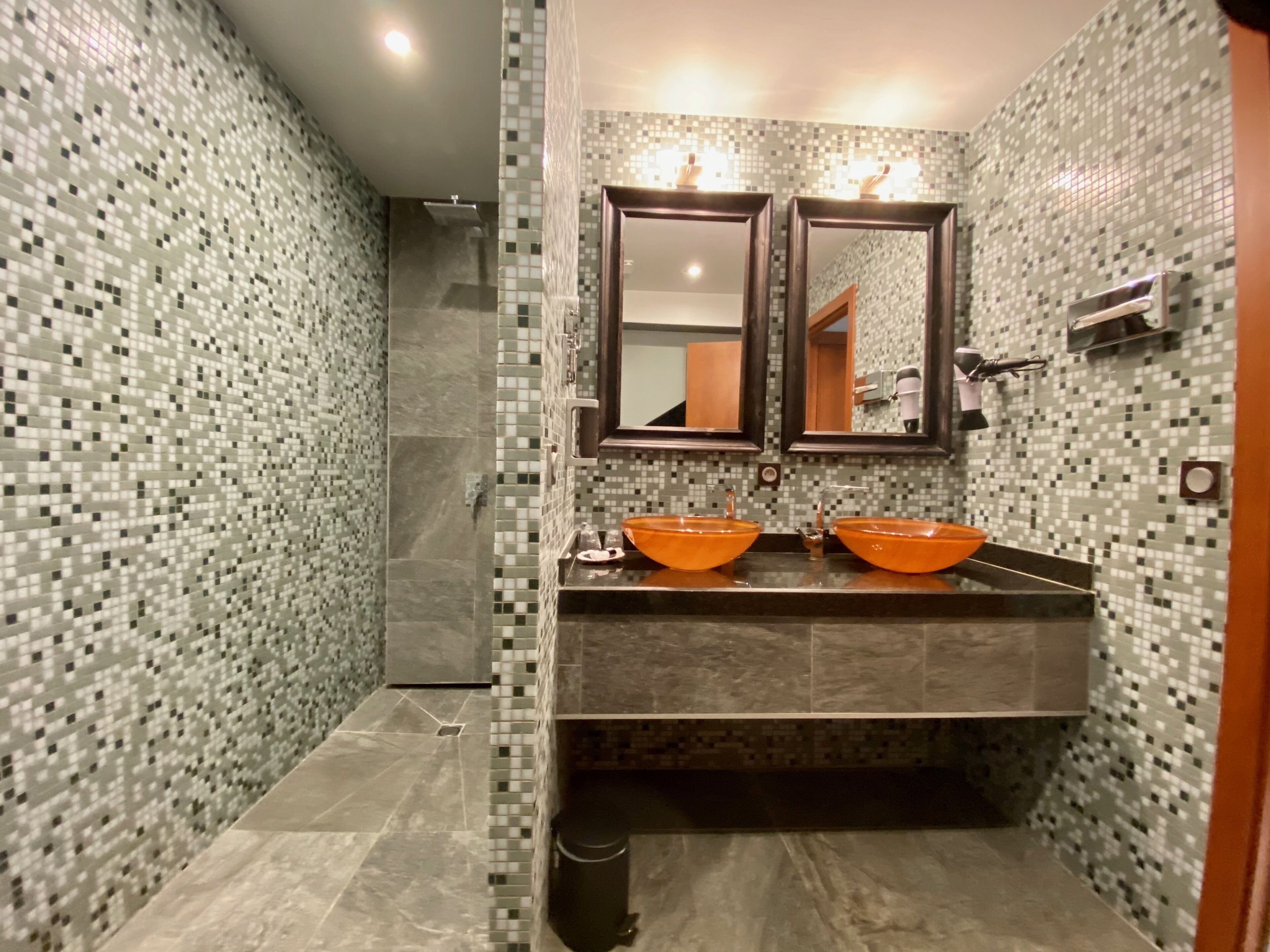 Une salle de bain avec des murs recouverts de mosaïques, deux lavabos orange, un miroir et un porte-serviettes.