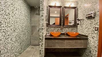 Une salle de bain avec des murs recouverts de mosaïques, deux lavabos orange, un miroir et un porte-serviettes.