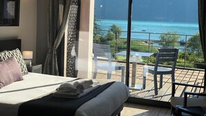 Een slaapkamer met een groot bed, uitzicht op zee en een balkon met stoelen en een tafel.