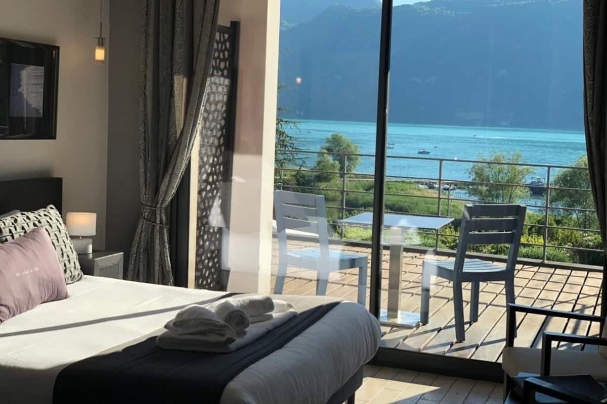Een slaapkamer met een groot bed, uitzicht op zee en een balkon met stoelen en een tafel.