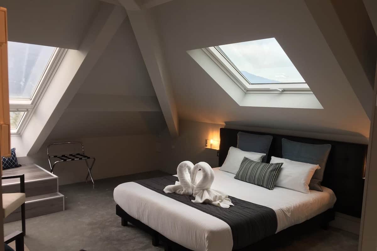 Een slaapkamer met dakraam, een bed met kussens, een nachtkastje en een stoel.