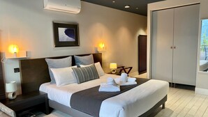 Een moderne hotelkamer met een groot bed, bedlampjes, een kunstwerk in een lijst aan de muur, en een airconditioning.