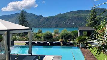 Relax by the serene pool overlooking the lake and mountains, surrounded by lush greenery and comfortable lounge chairs.