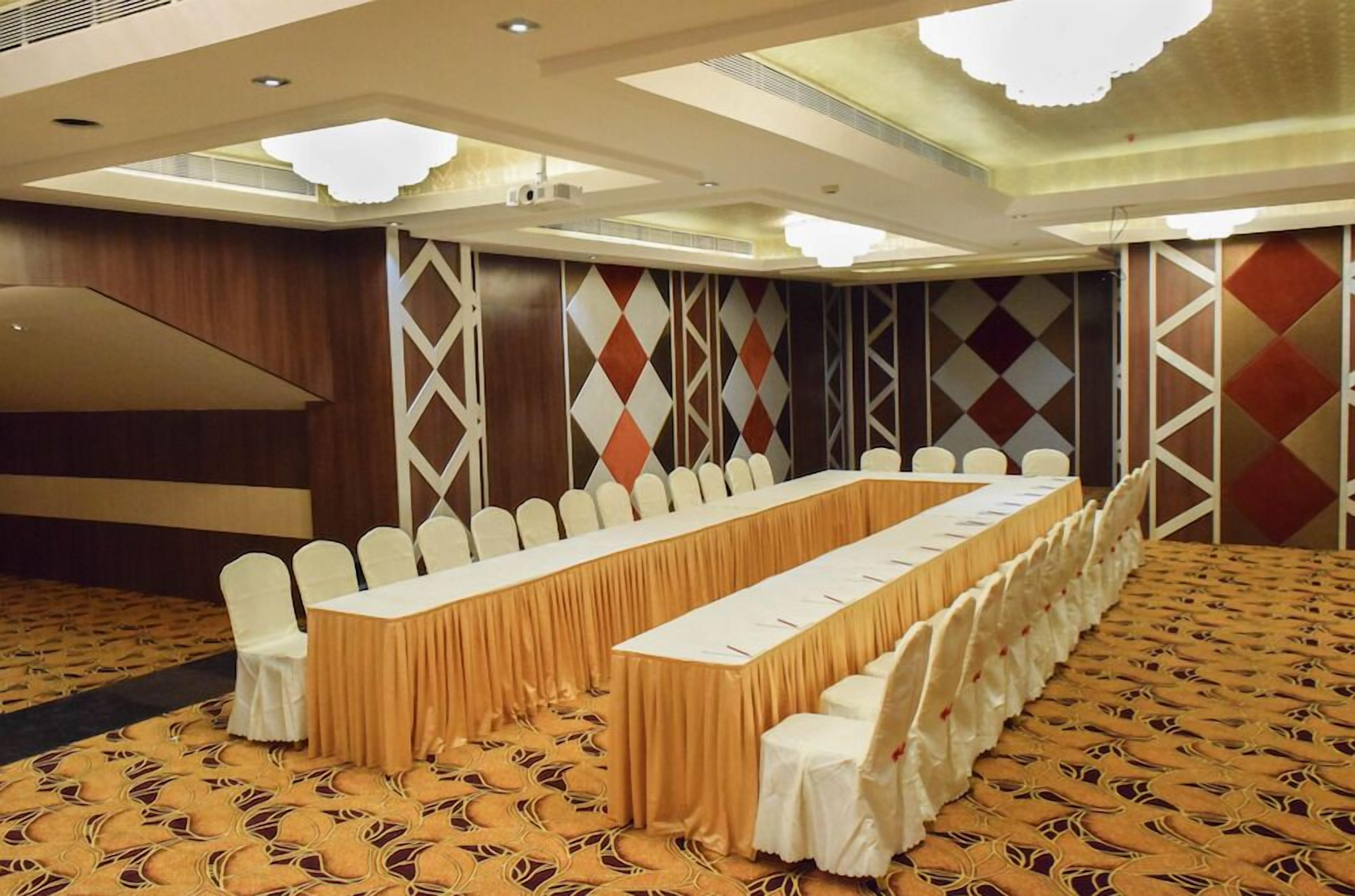 Une salle de conférence avec une longue table, des chaises blanches et un tapis à motifs.