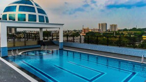 A rooftop pool with a blue and white dome structure, surrounded by a black fence and overlooking a cityscape with high-rise buildings. - RG Royal Hotel and Convention (Bengaluru)