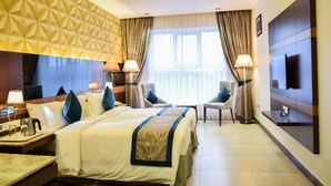 A hotel room with two beds, a TV, a desk with a lamp, and a view of the outdoors through large windows. - RG Royal Hotel and Convention (Bengaluru)