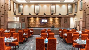 A hotel lobby with a reception desk, multiple dining tables, and orange patterned chairs. - RG Royal Hotel and Convention (Bengaluru)