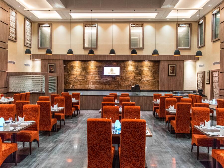 Un vestíbulo de hotel con mostrador de recepción, varias mesas de comedor y sillas con estampado naranja.