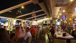 An outdoor dining area with tables and chairs, surrounded by a covered patio with a patterned ceiling. - Mitos App & Hotel (Alanya)