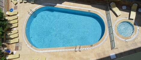 Et rektangulært swimmingpool med tilhørende terrasse, liggestole og jacuzzi.