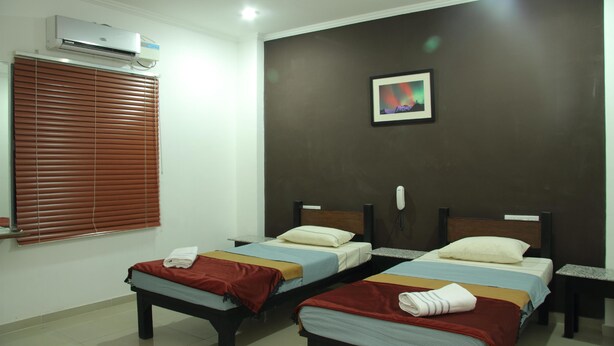 A hotel room with two beds, a ceiling fan, an air conditioning unit, a framed picture on the wall, and a telephone on the nightstand. - Deccan Comforts (Hyderabad)