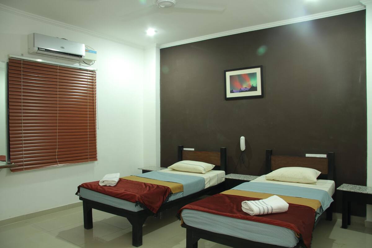 A hotel room with two beds, a ceiling fan, an air conditioning unit, a framed picture on the wall, and a telephone on the nightstand.