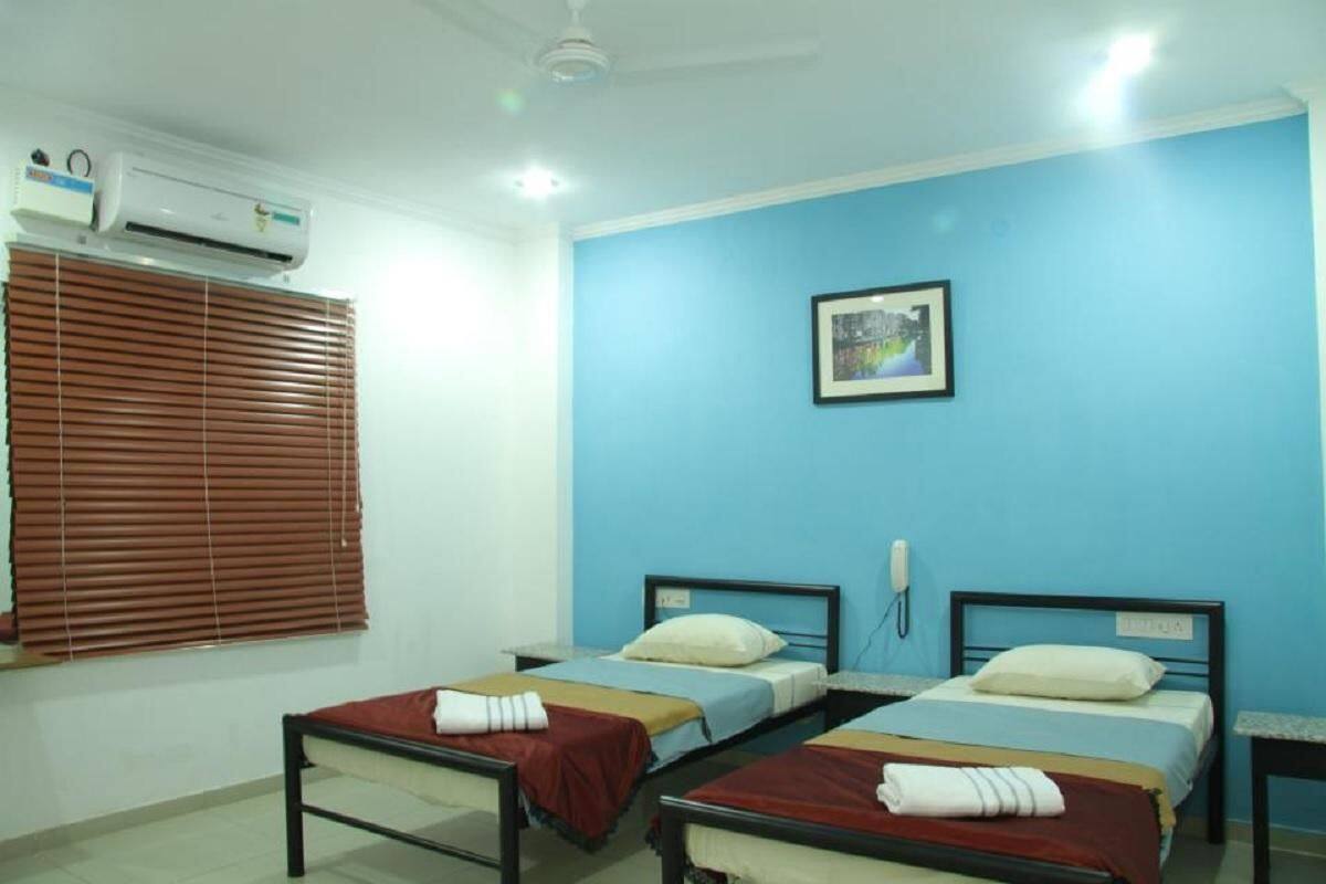 A room with two beds, an air conditioning unit, a window with blinds, and a wall-mounted phone.