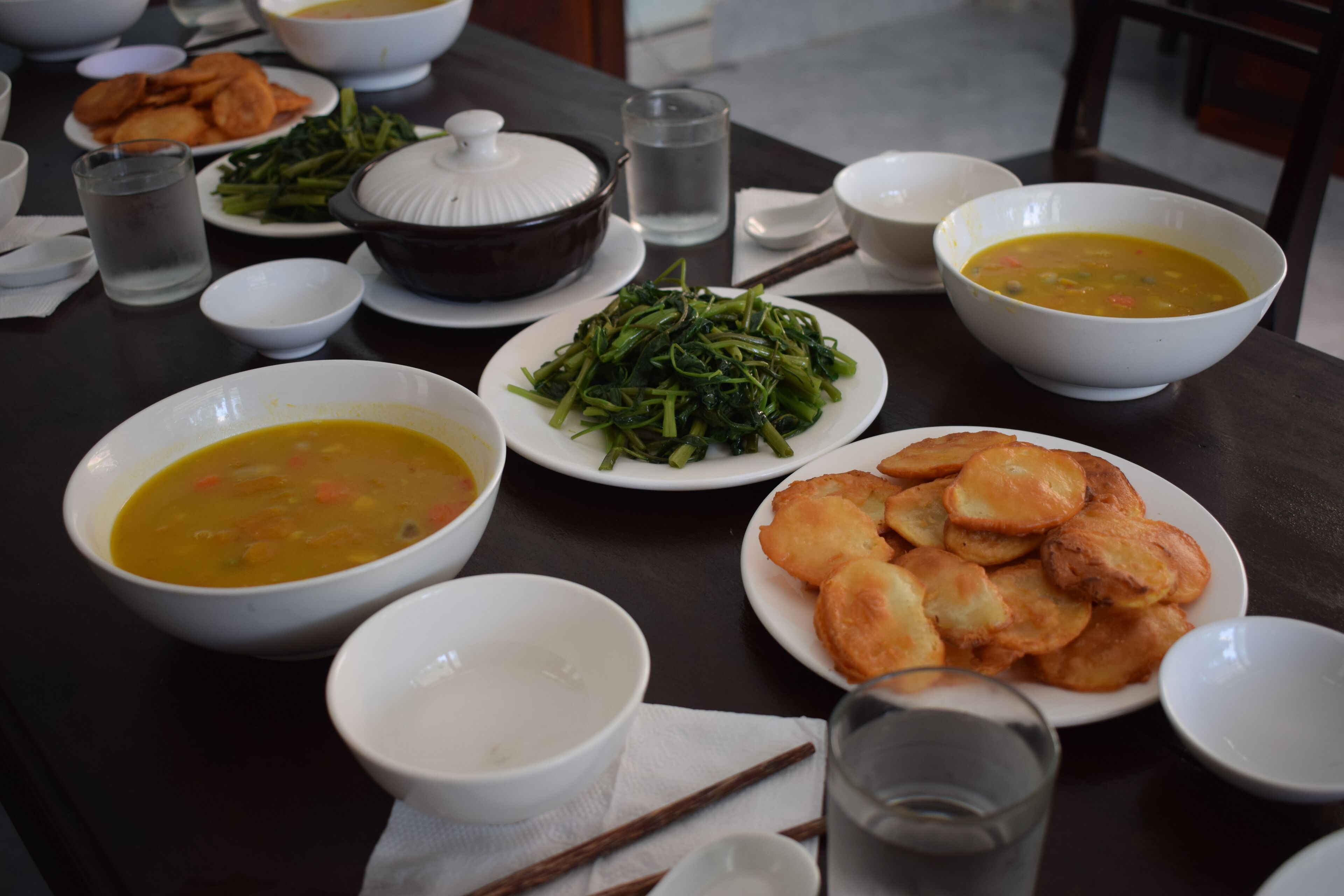 A dining table with various dishes including soup, greens, and fried items.