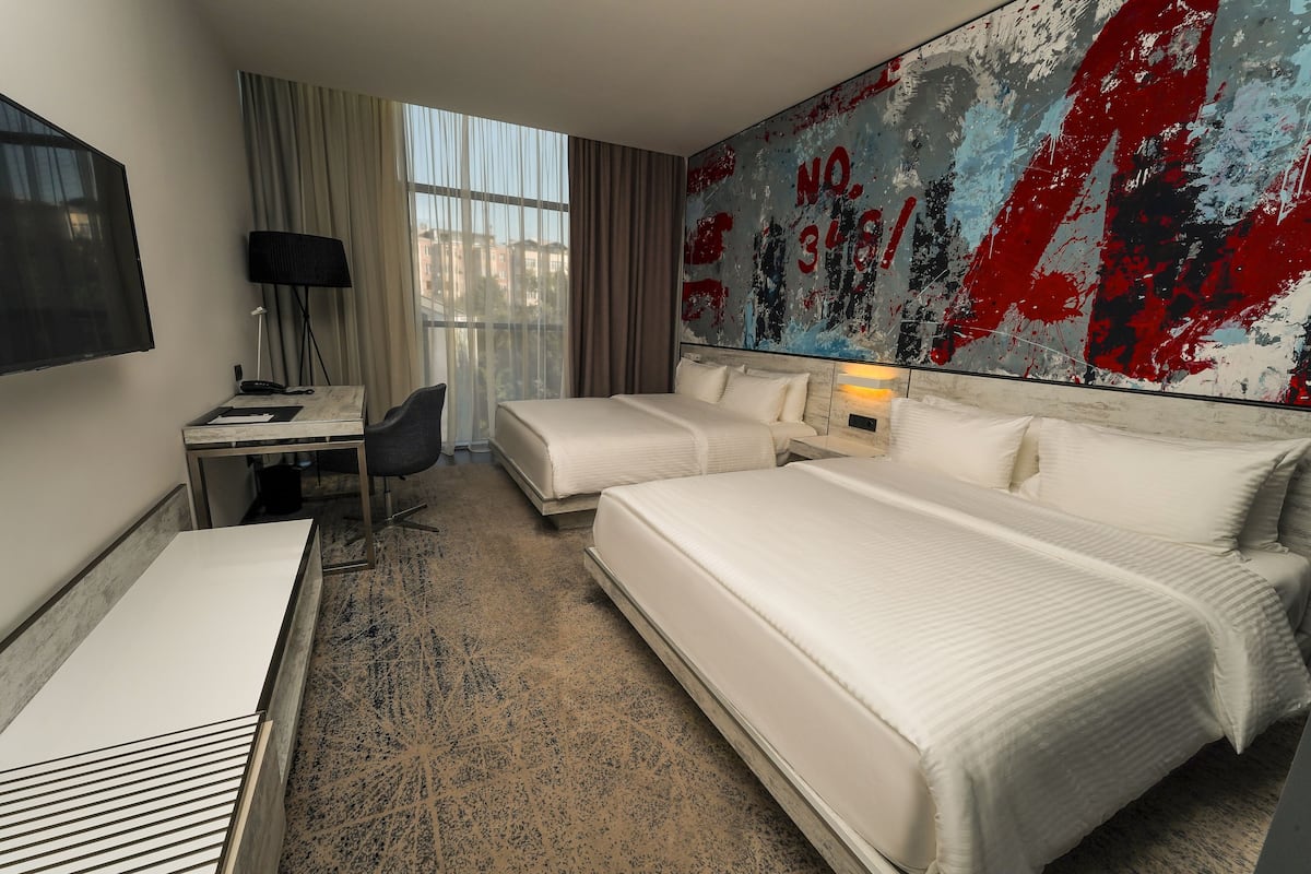 Een hotelkamer met twee bedden, een bureau, een stoel, een televisie en een groot abstract schilderij aan de muur.