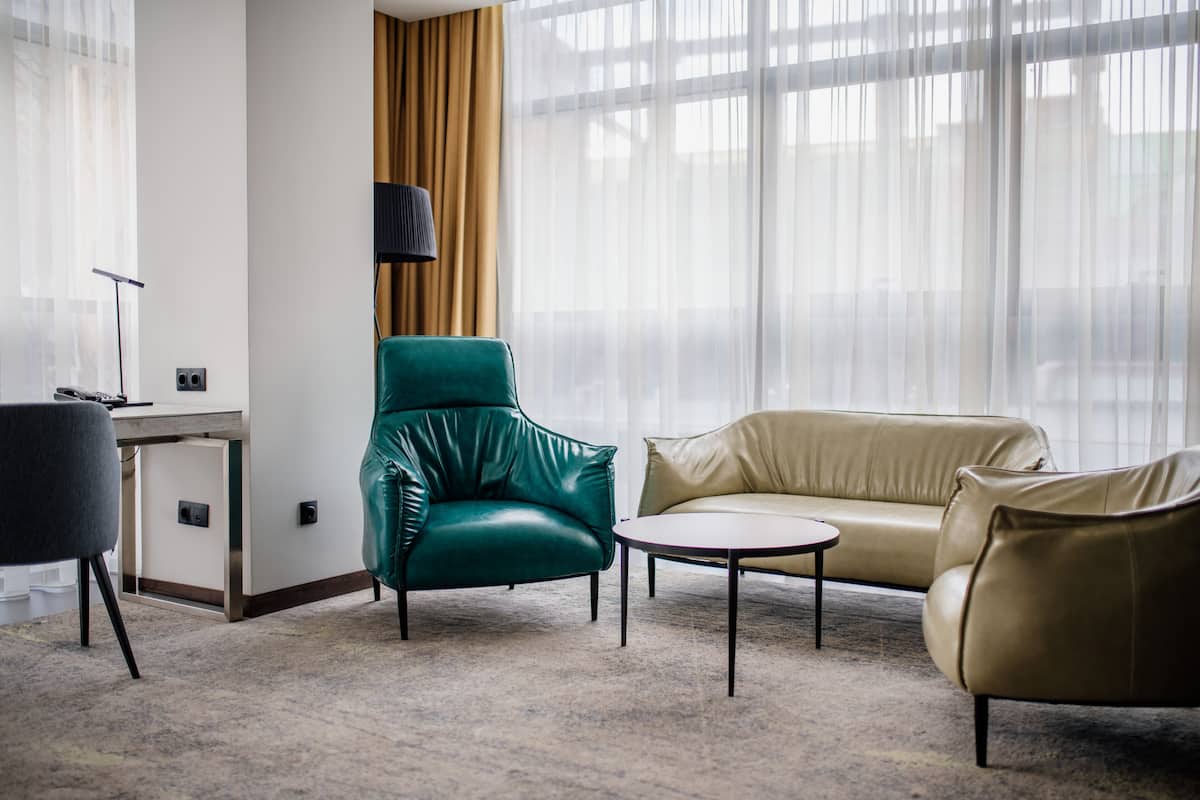 Een moderne woonkamer met een groene fauteuil, een beige bank en een kleine ronde tafel.