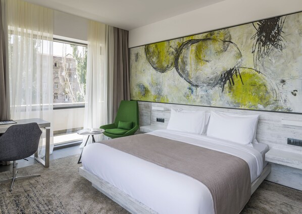 A modern hotel room with a large bed, a green armchair, a small table, and a large abstract painting on the wall. - Messier 53 Hotel Yerevan (Yerevan)