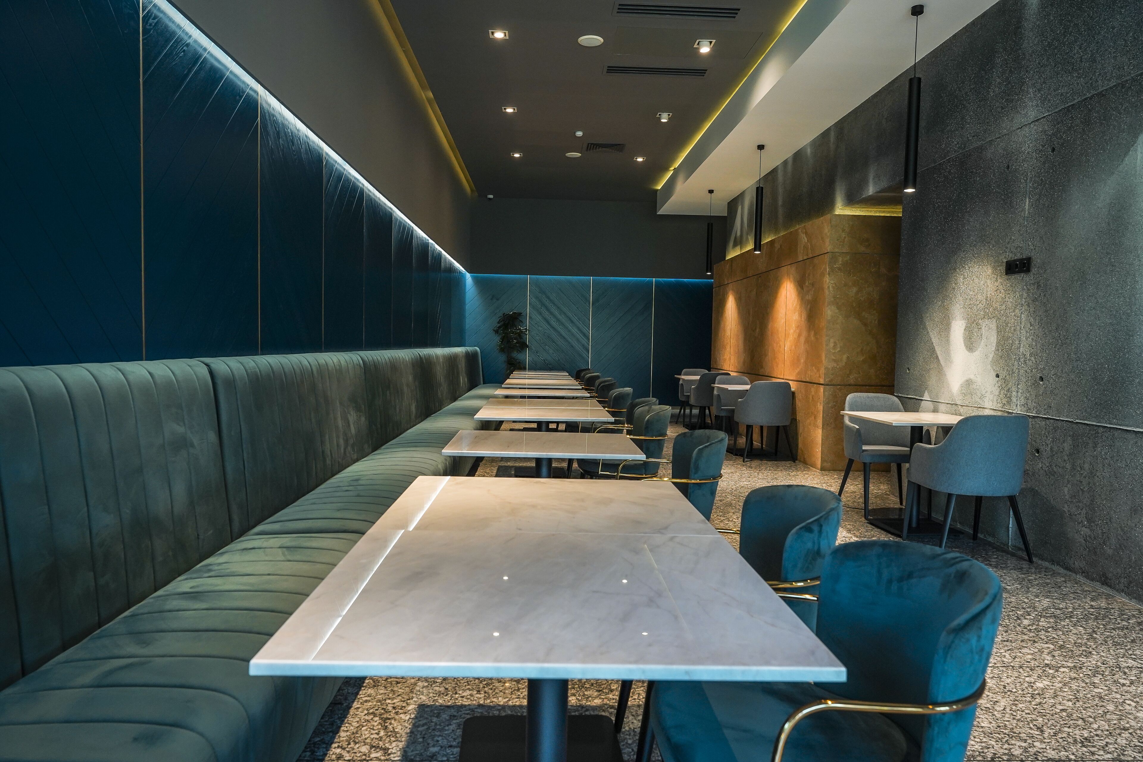 A modern restaurant with a long counter, green upholstered booths, and a mix of seating options.