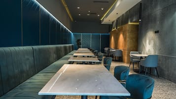 A modern restaurant with a long counter, green upholstered booths, and a mix of seating options.