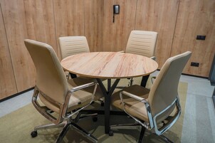 Een vergaderzaal met een ronde tafel en vier beige stoelen met metalen poten.