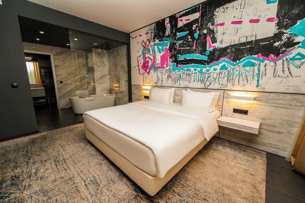 Een moderne slaapkamer met een groot bed, marmeren wanden en een kleurrijk abstract schilderij.