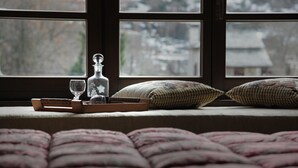 Un lit recouvert d’une couette rose, une table de chevet avec une bouteille et un verre, et une fenêtre donnant sur des immeubles.