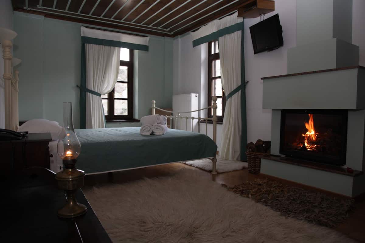 A bedroom with a bed, a fireplace, and a desk with a lamp.