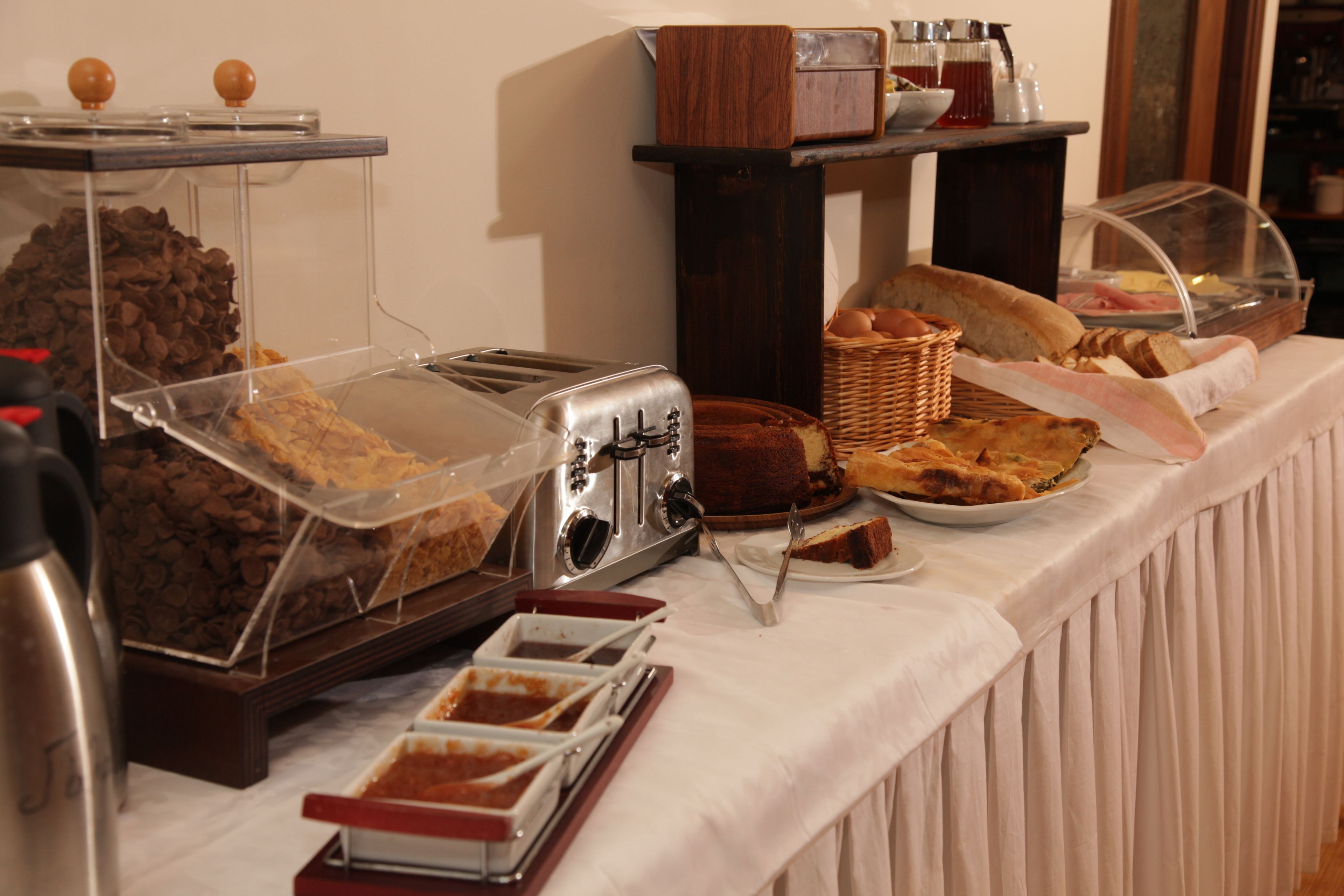 A buffet table with various food items, including bread, pastries, and a cake, covered with clear plastic.