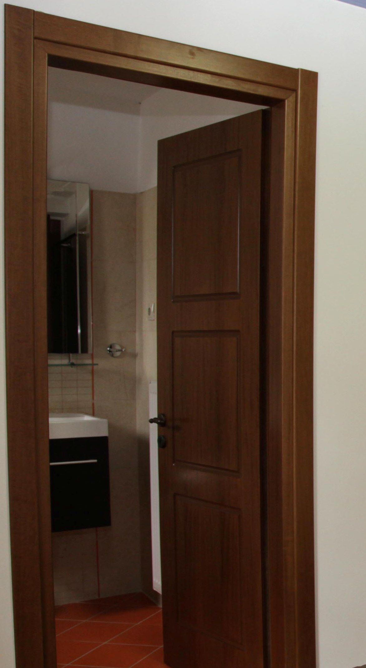 A wooden door leading to a bathroom with a white sink and a mirror.