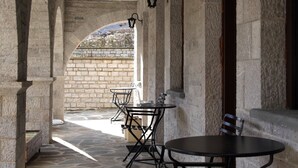Un couloir dallé de pierres, avec des tables et des chaises, des murs en pierre et une vue sur un jardin.