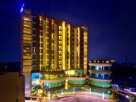 A multi-story hotel with a modern design, featuring balconies and a landscaped garden area.