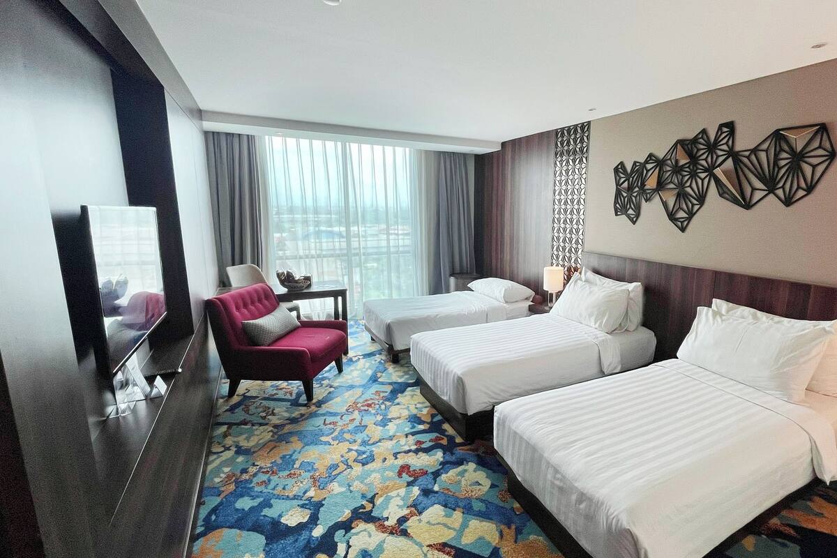 Een hotelkamer met twee bedden, een rode fauteuil, een tafeltje en een grote spiegel.