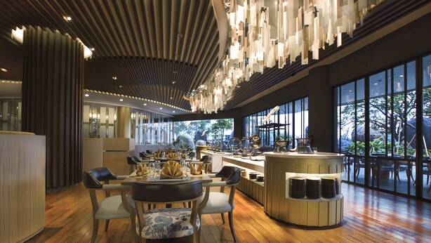 Un restaurant moderne doté d’un plancher en bois, d’une grande table à manger centrale entourée de chaises et d’un bar avec des tabourets.