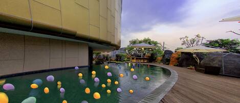 A swimming pool with colorful floating objects, a wooden deck, and a building in the background.