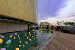 A swimming pool with colorful floating objects, a wooden deck, and a building in the background.