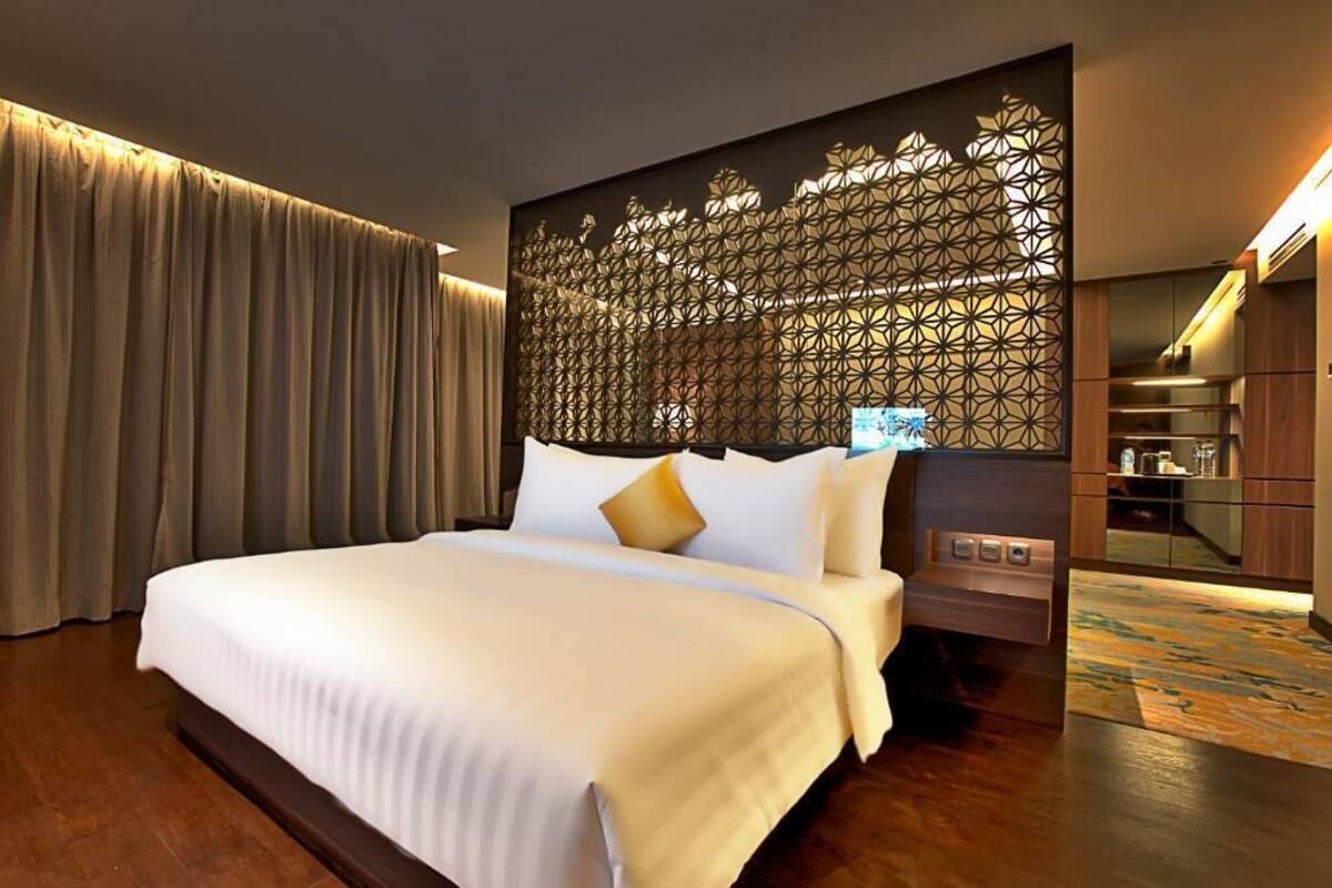 Hotelkamer met een groot bed, een decoratieve scheidingswand, een minibar en uitzicht op de keukenruimte.