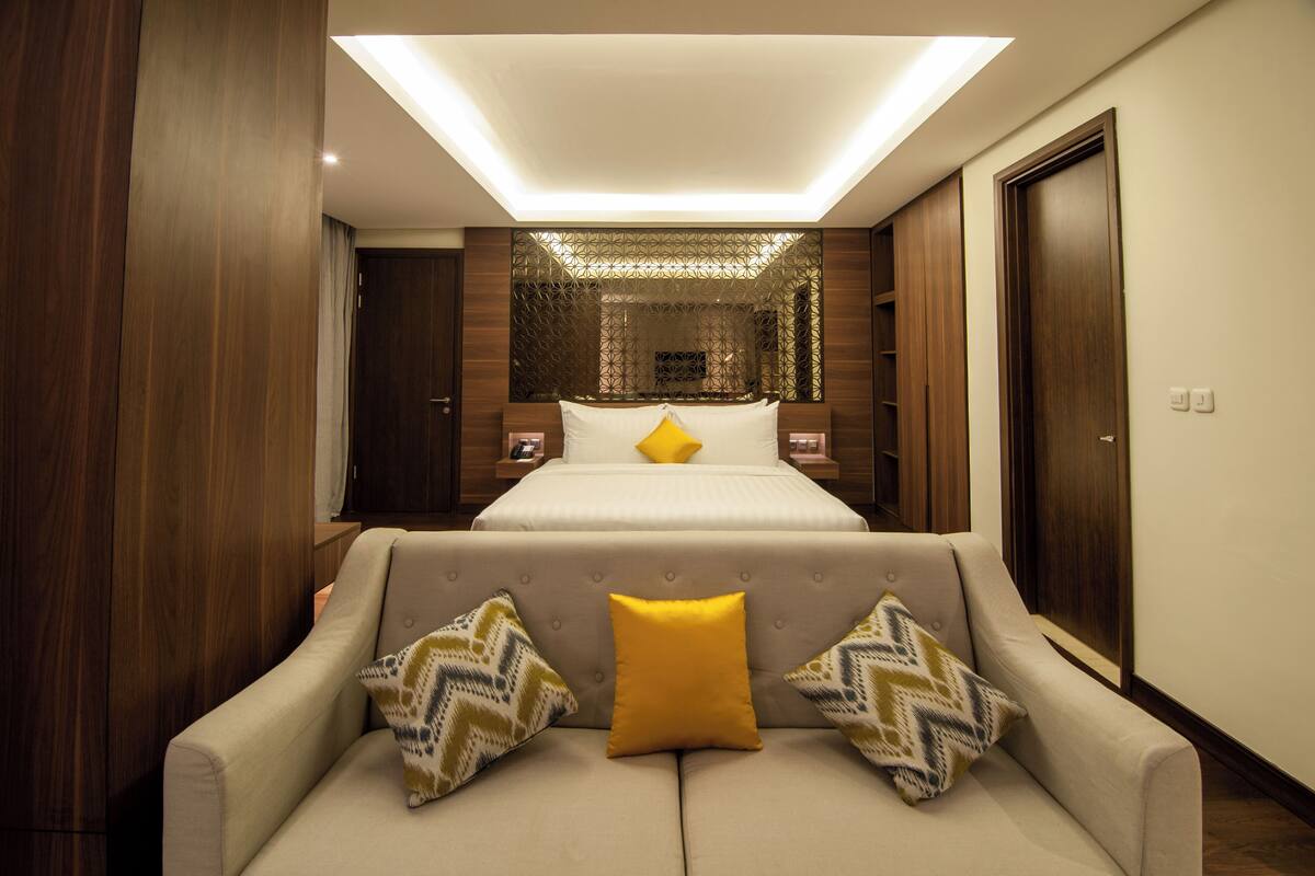 Een moderne hotelkamer met een groot bed, een bank met opvallende kussens en een dakraam boven het bed.