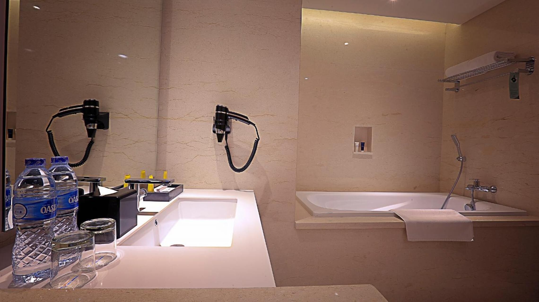 Une salle de bain moderne avec un grand lavabo blanc, deux sèche-cheveux fixés au mur, une baignoire et une douche.
