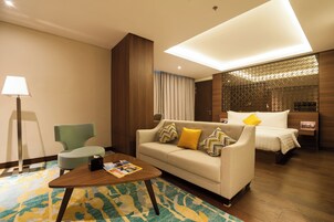 A hotel room with a sofa, a small table with a magazine, a lamp, a bed with pillows, and a decorative partition.
