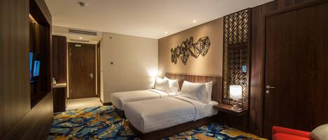 A hotel room with two beds, a TV, a desk with a lamp, and a red chair.
