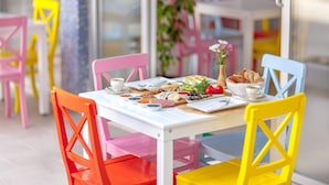Un comedor de colores vivos con una mesa blanca dispuesta para una comida, rodeada de sillas multicolores.