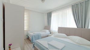 Habitación de hotel con dos camas, una mesita con un florero y velas, y una ventana con cortinas.