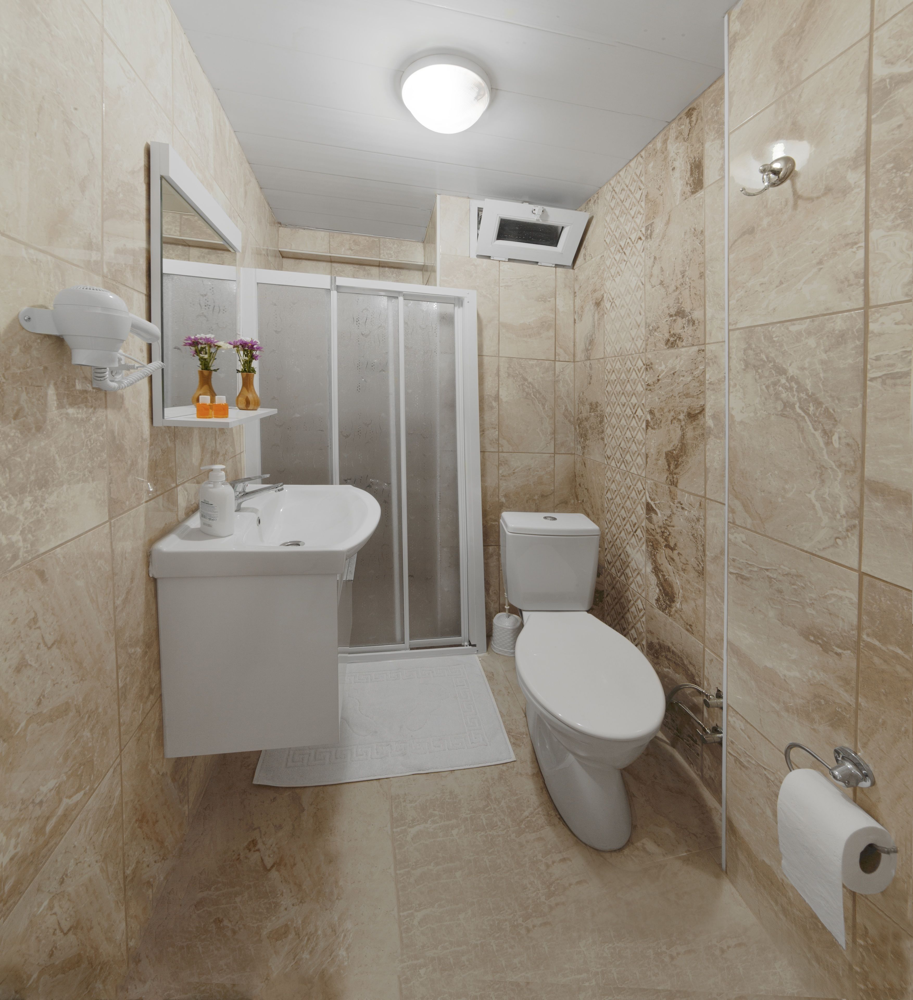 A bathroom with a shower, toilet, sink, and a hairdryer mounted on the wall.