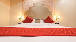 Habitación de hotel con una cama grande, ropa de cama roja y blanca, dos almohadas rojas, un cabecero decorativo y lámparas fijadas a la pared.
